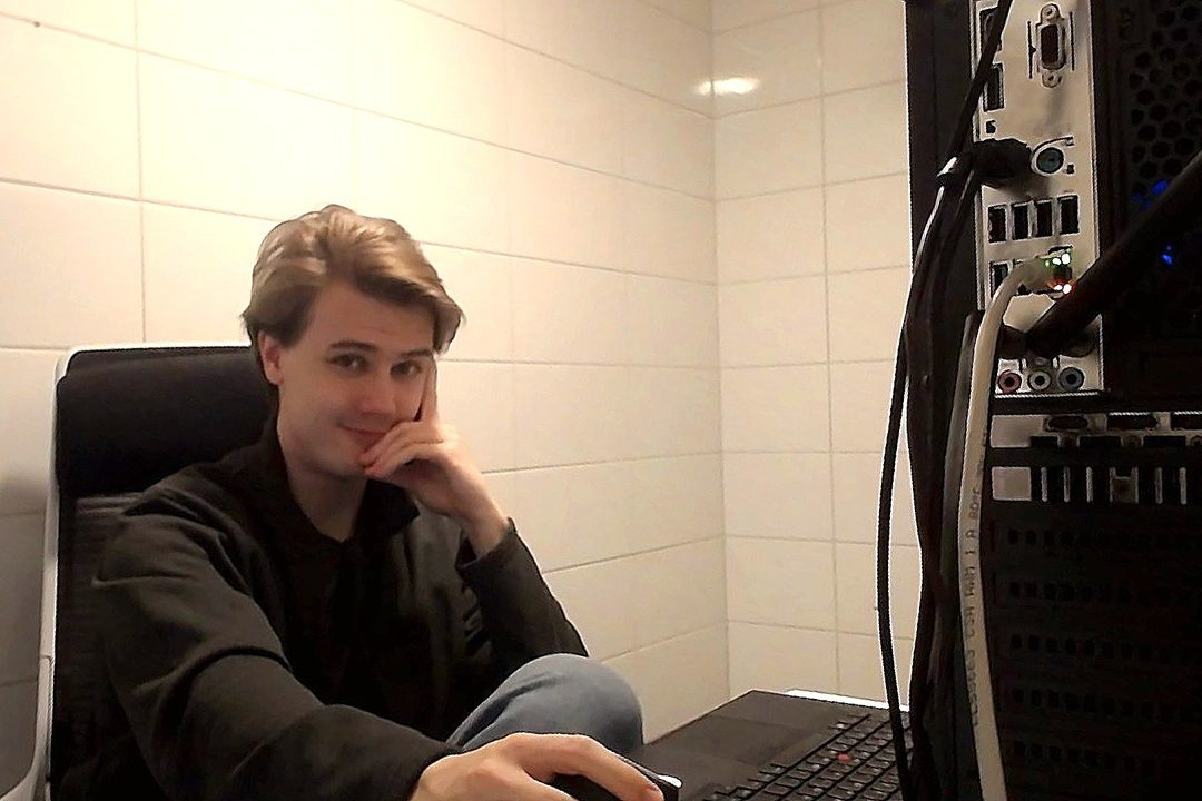 Pietari at his desk in a tiled bathroom, next to a PC full of cables